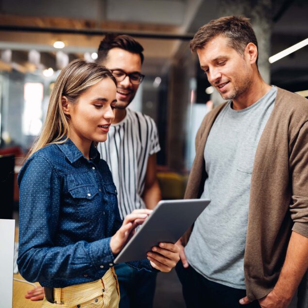 Three office workers standing together looking at a mobile device.