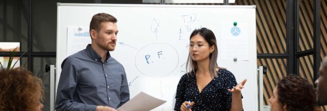 Two people standing in front of a whiteboard having a meeting.