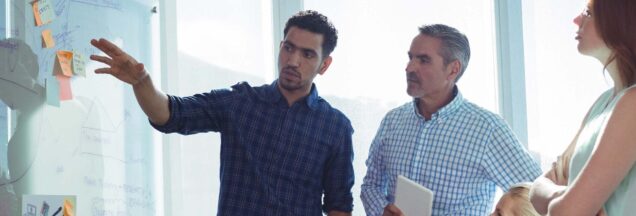 Three people having a meeting next to a whiteboard.